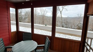 Ein überdachter Außenbereich mit Tisch und Stühlen, einem Deckenventilator und großen Fenstern, die einen Blick auf eine verschneite Landschaft bieten.