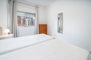 Een hotelkamer met twee bedden, een houten dressoir, een raam met uitzicht op gebouwen en een spiegel aan de muur.