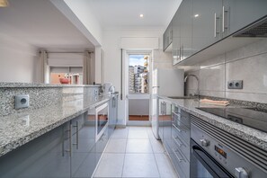 Een moderne keuken met granieten aanrecht, roestvrijstalen apparatuur en uitzicht door een open deur naar een balkon.