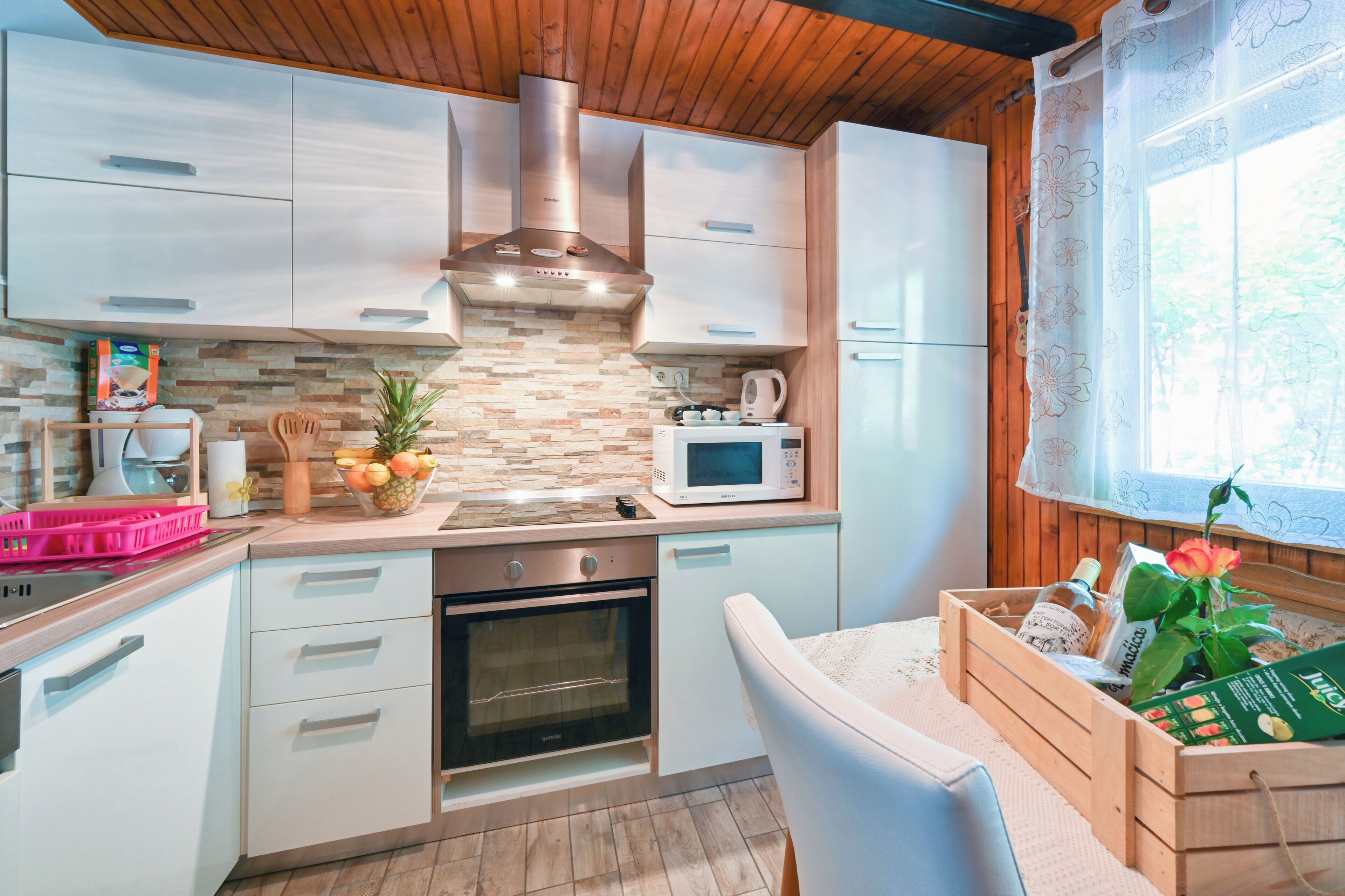 A modern kitchen with white cabinets, a stainless steel range hood, a microwave, and a wooden countertop.