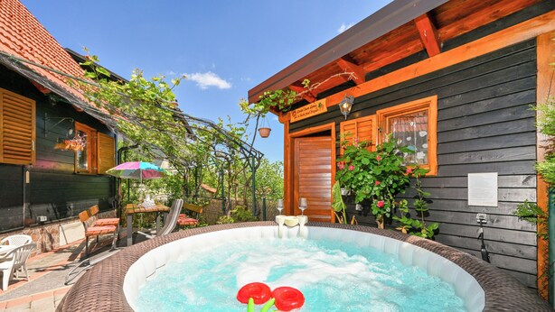 Un jacuzzi rodeado de muebles de mimbre, una terraza de madera y un edificio con techo rojo.