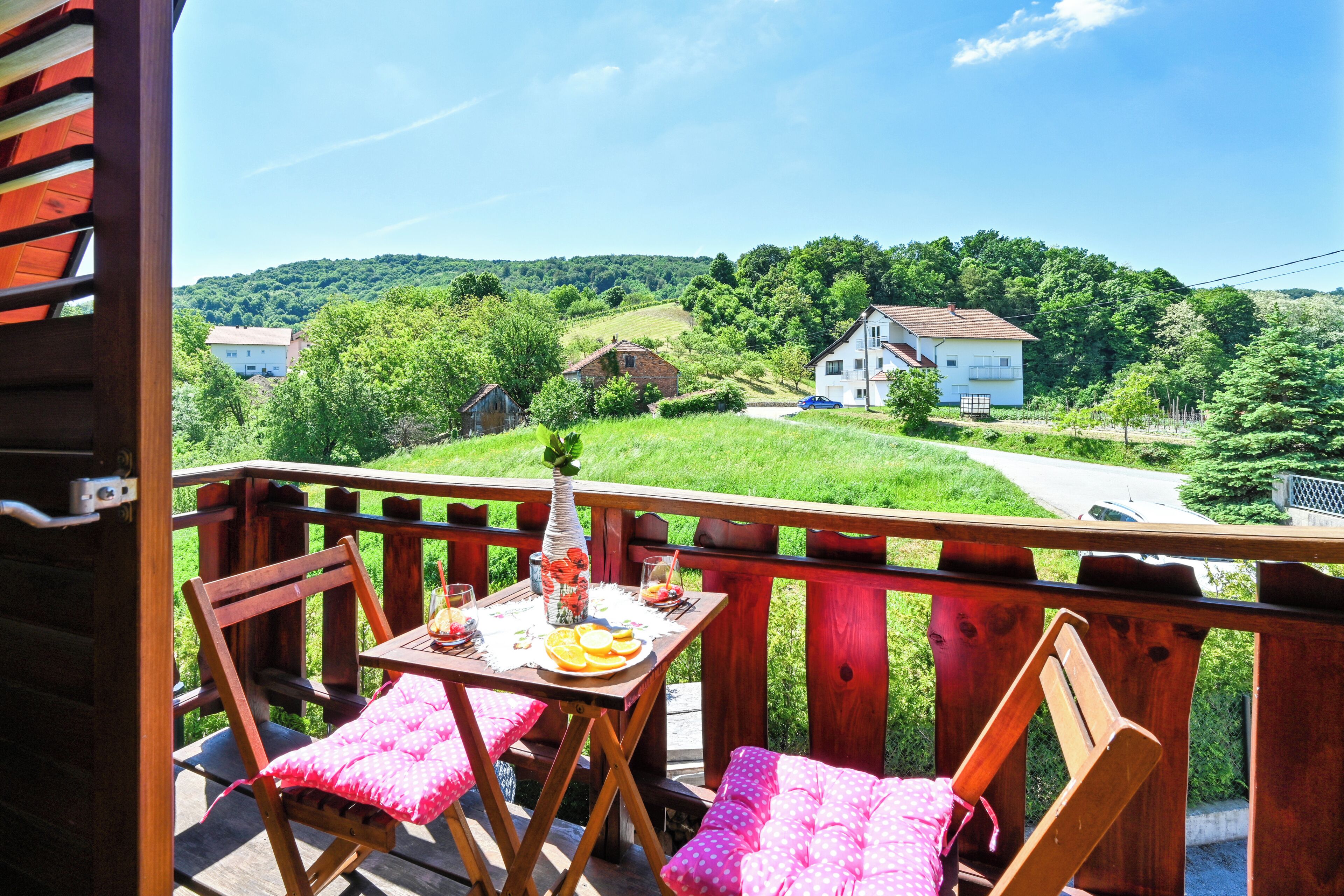 Una terraza de madera con una mesa y sillas, con vistas a un paisaje verde con casas.