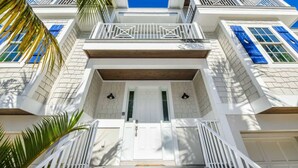 A multi-story building with white exterior walls, blue shutters, and a central entrance with a white door. - Malibu Beach ~ Waterslide/Rooftop Views/Walk to Beach (Holmes Beach)