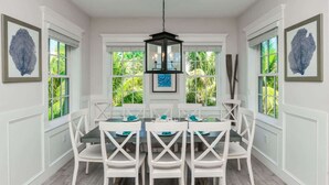 A dining area with a round table, white chairs, and a black hanging light fixture. - Malibu Beach ~ Waterslide/Rooftop Views/Walk to Beach (Holmes Beach)