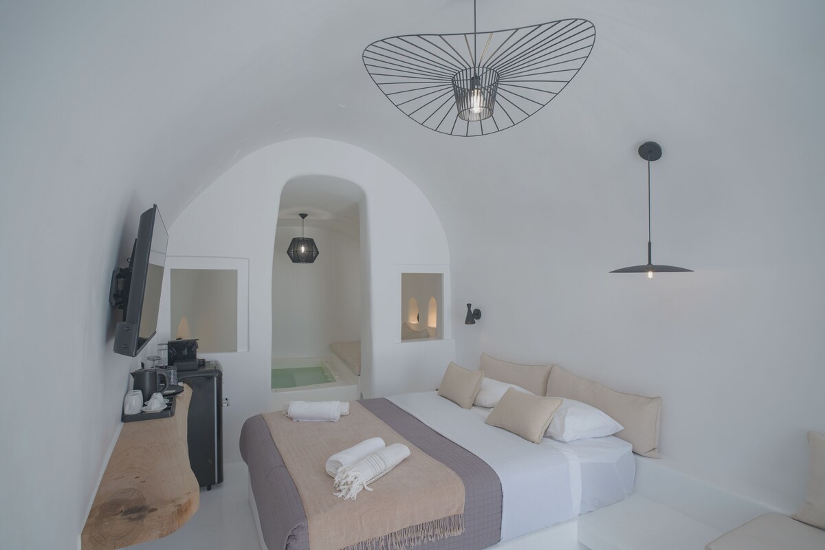 A modern bedroom with a bed, a desk, a mirror, and a shower area.