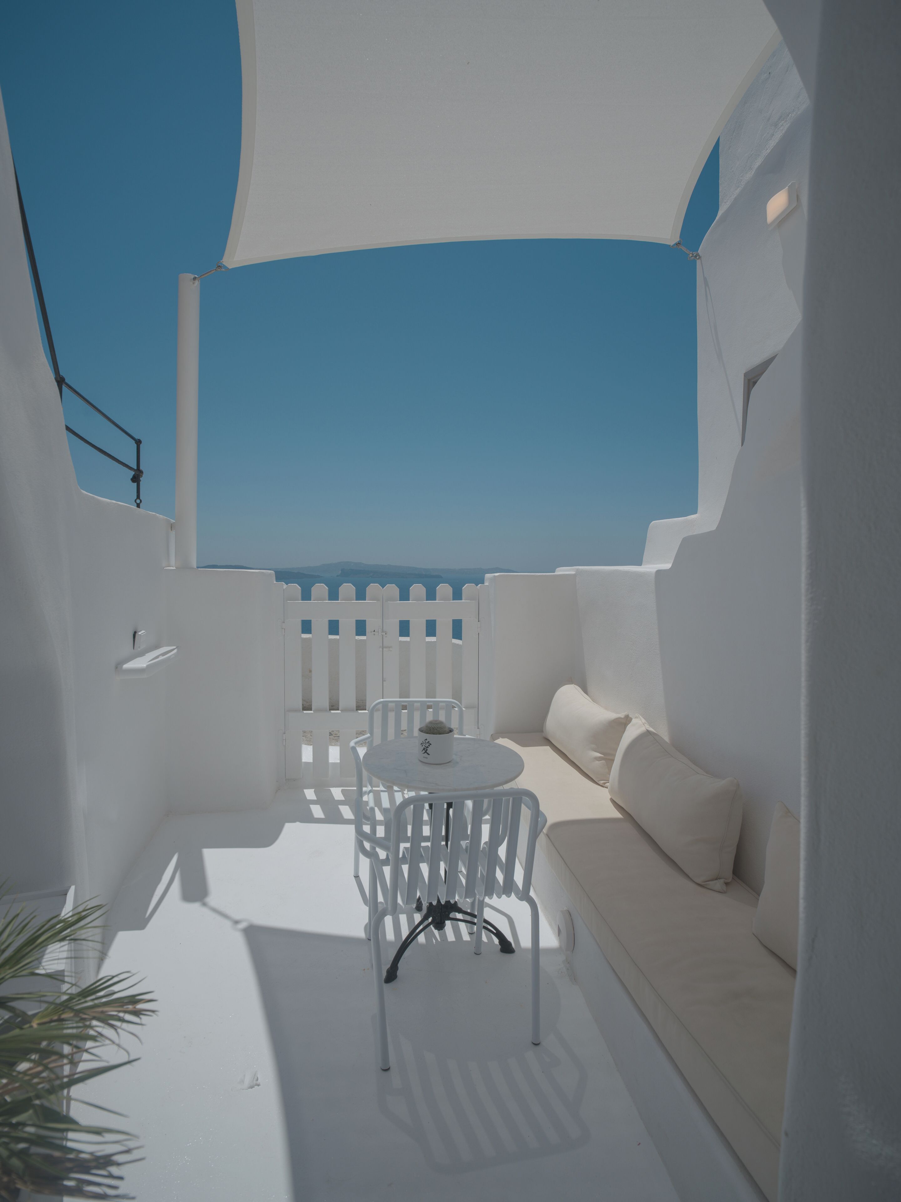 A white outdoor seating area with a table and chairs, a white sofa, and a white railing.