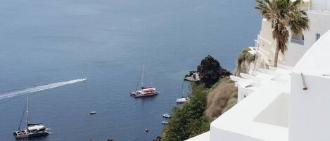 A coastal scene with white buildings, a rocky outcrop, and several boats on the water.