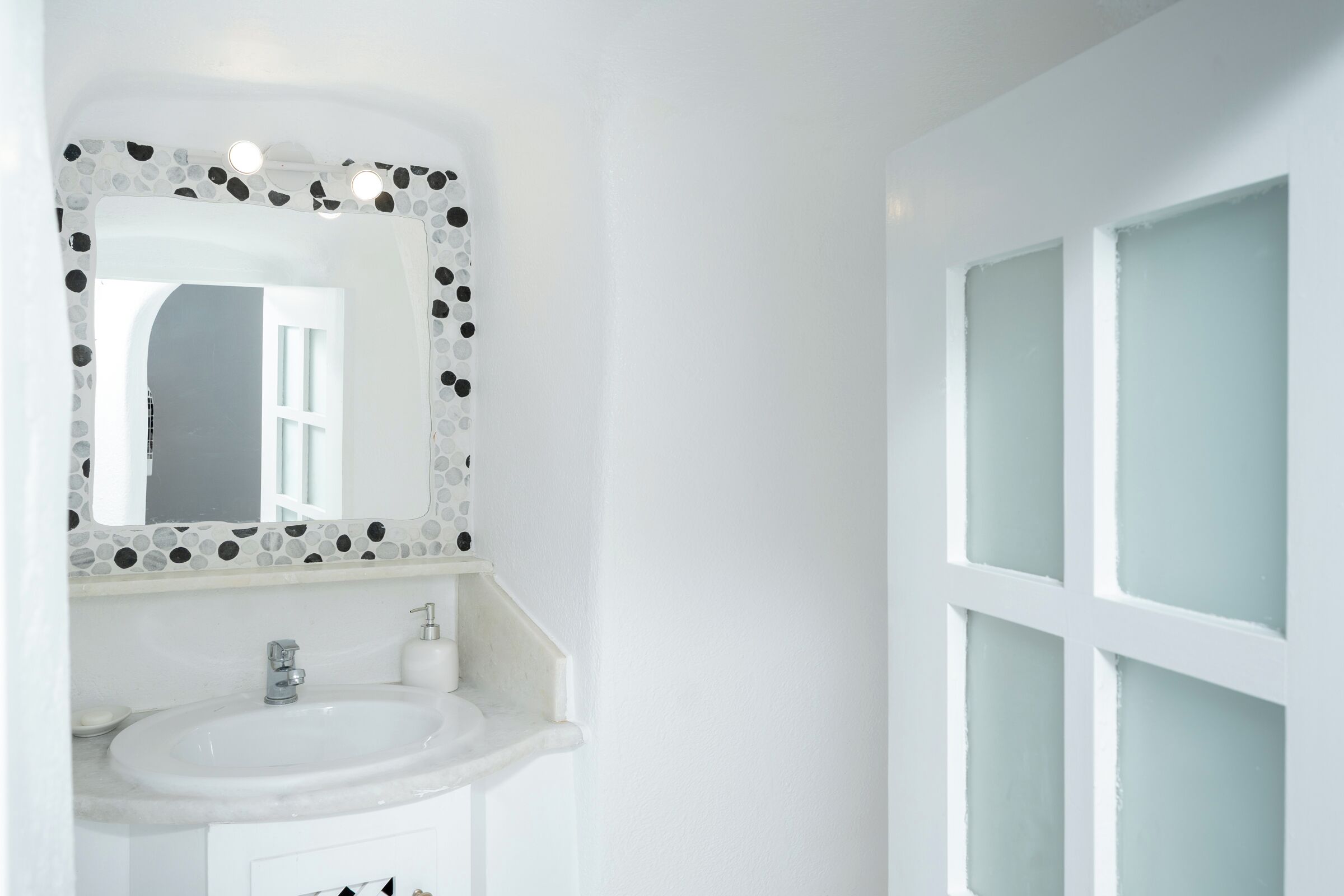 A bathroom with a white sink, a mirror with a mosaic border, and frosted glass windows.