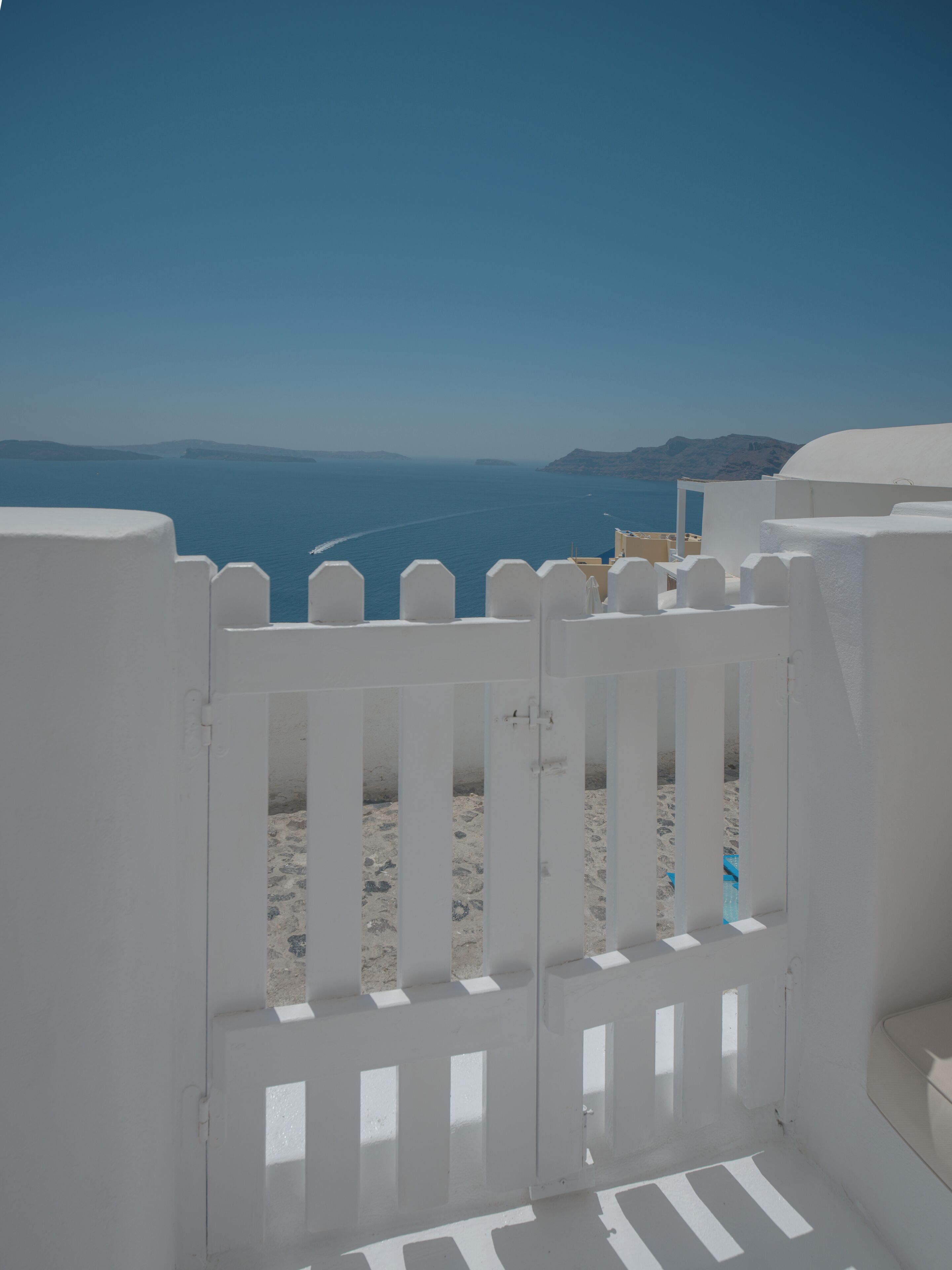 A white gate leading to a beach with a clear view of the sea and distant mountains.