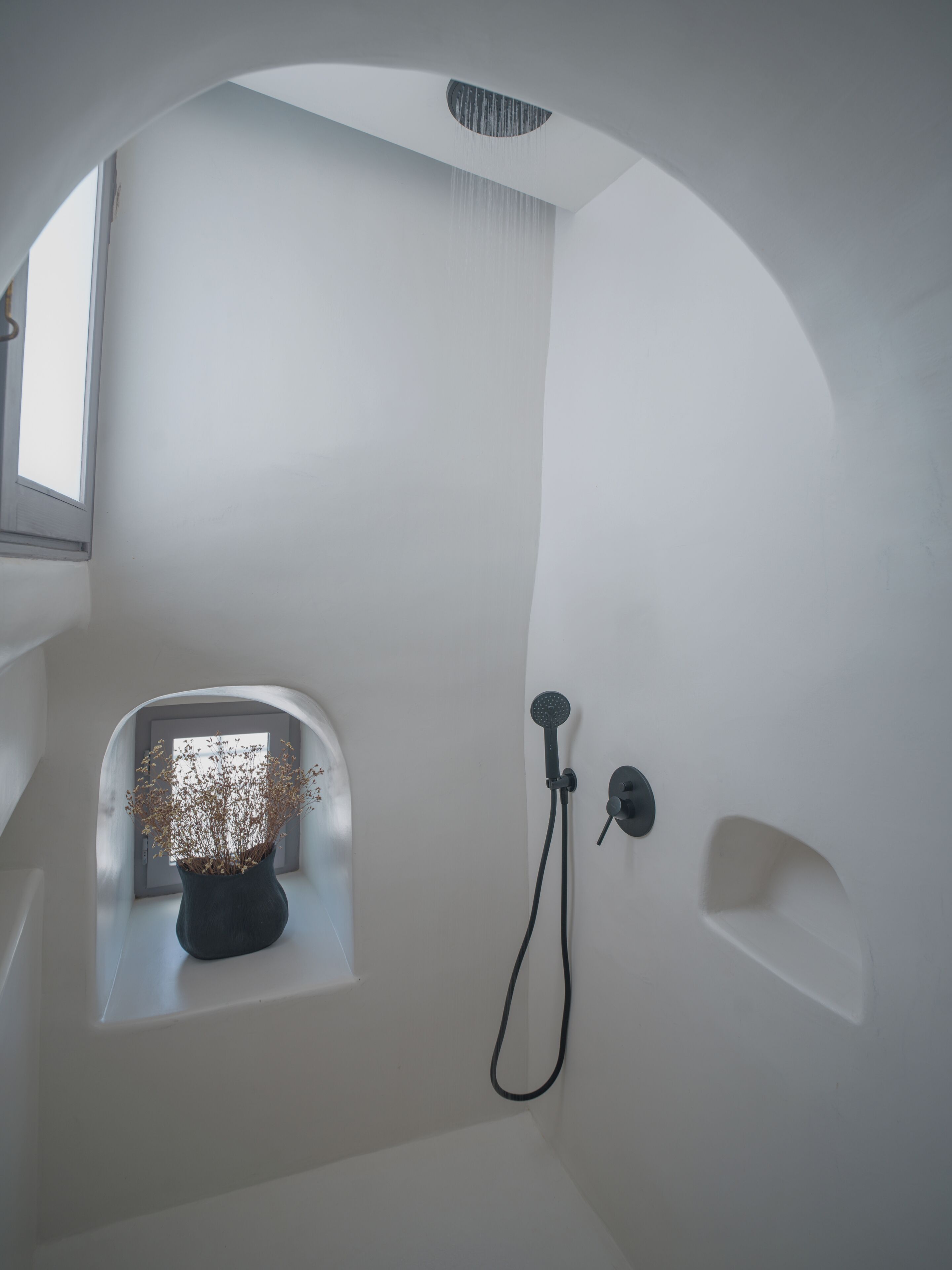 A modern bathroom with a shower, a small window with a plant, and a curved ceiling.