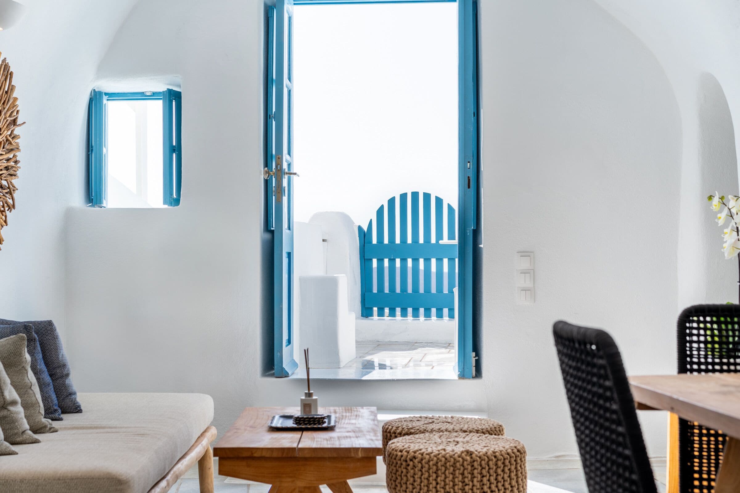 Ein Zimmer mit einem Holztisch, einem Sofa, einem Stuhl und einem Fenster mit Blick auf einen blauen Zaun.
