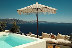 Une piscine avec vue sur la mer, un parasol blanc et un canapé avec des coussins.