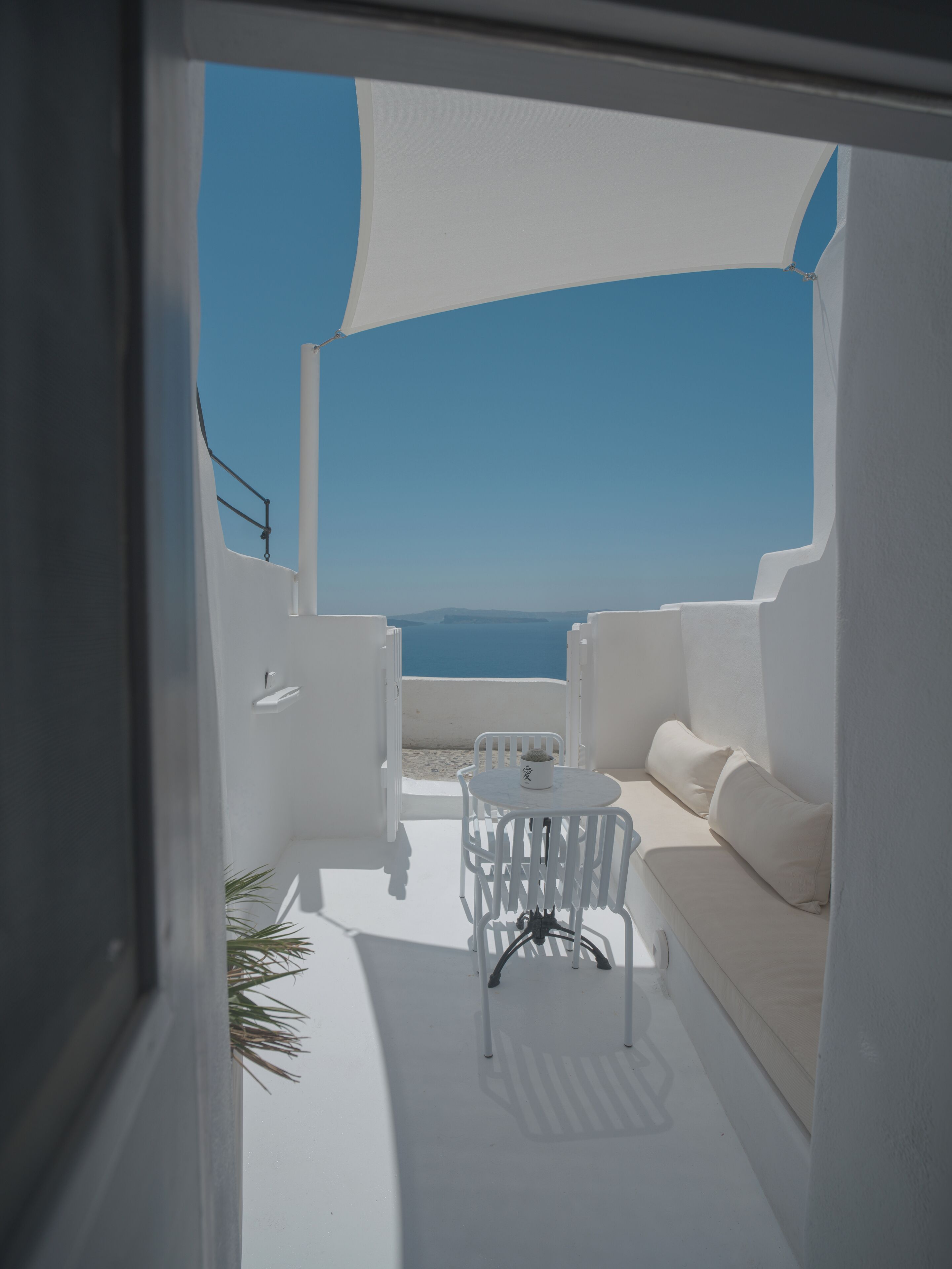 A white outdoor seating area with a table and chairs, a sofa, and a view of the sea.