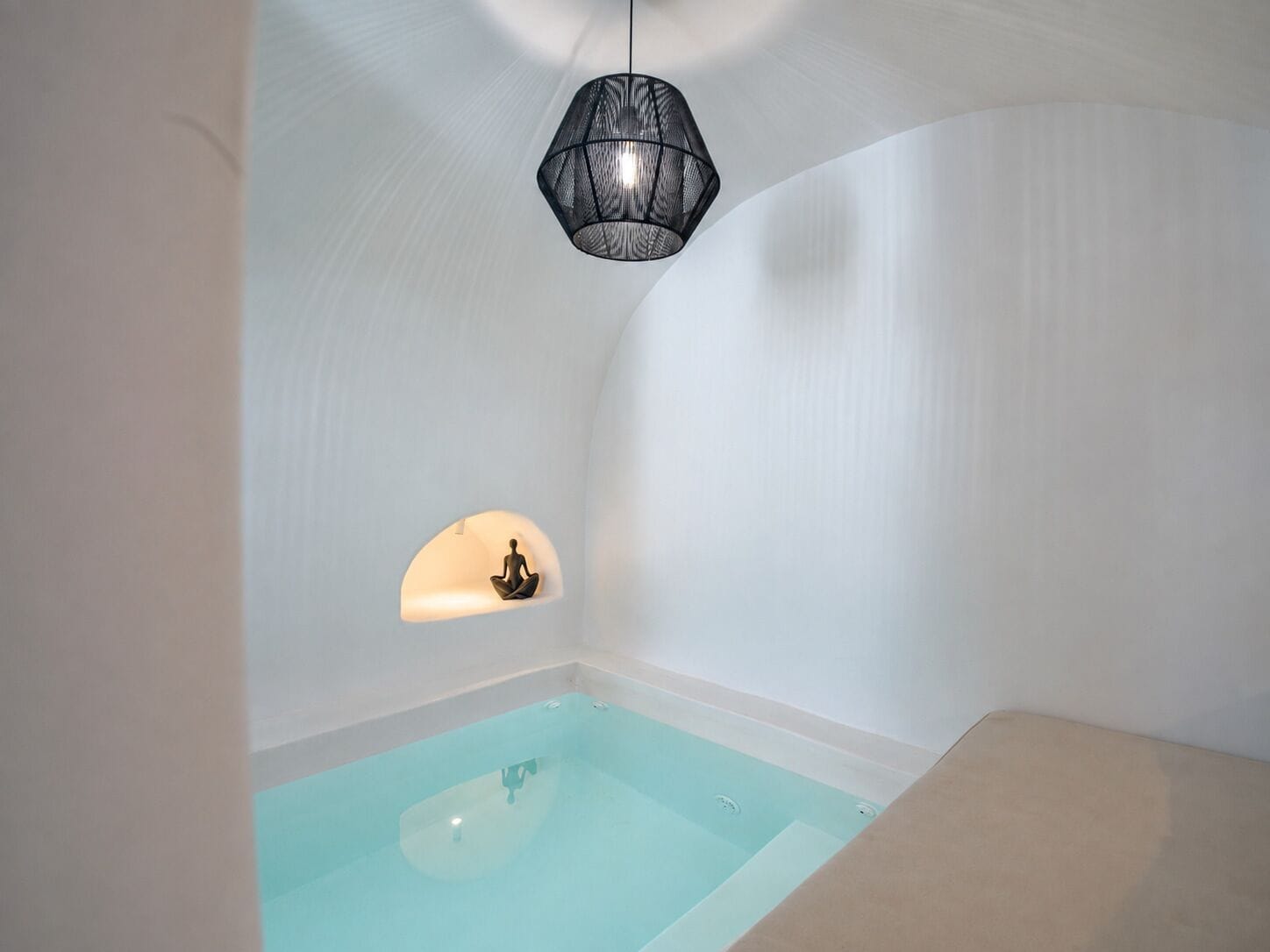 Habitación minimalista con una bañera, una lámpara colgante y una estantería de pared con una figura.