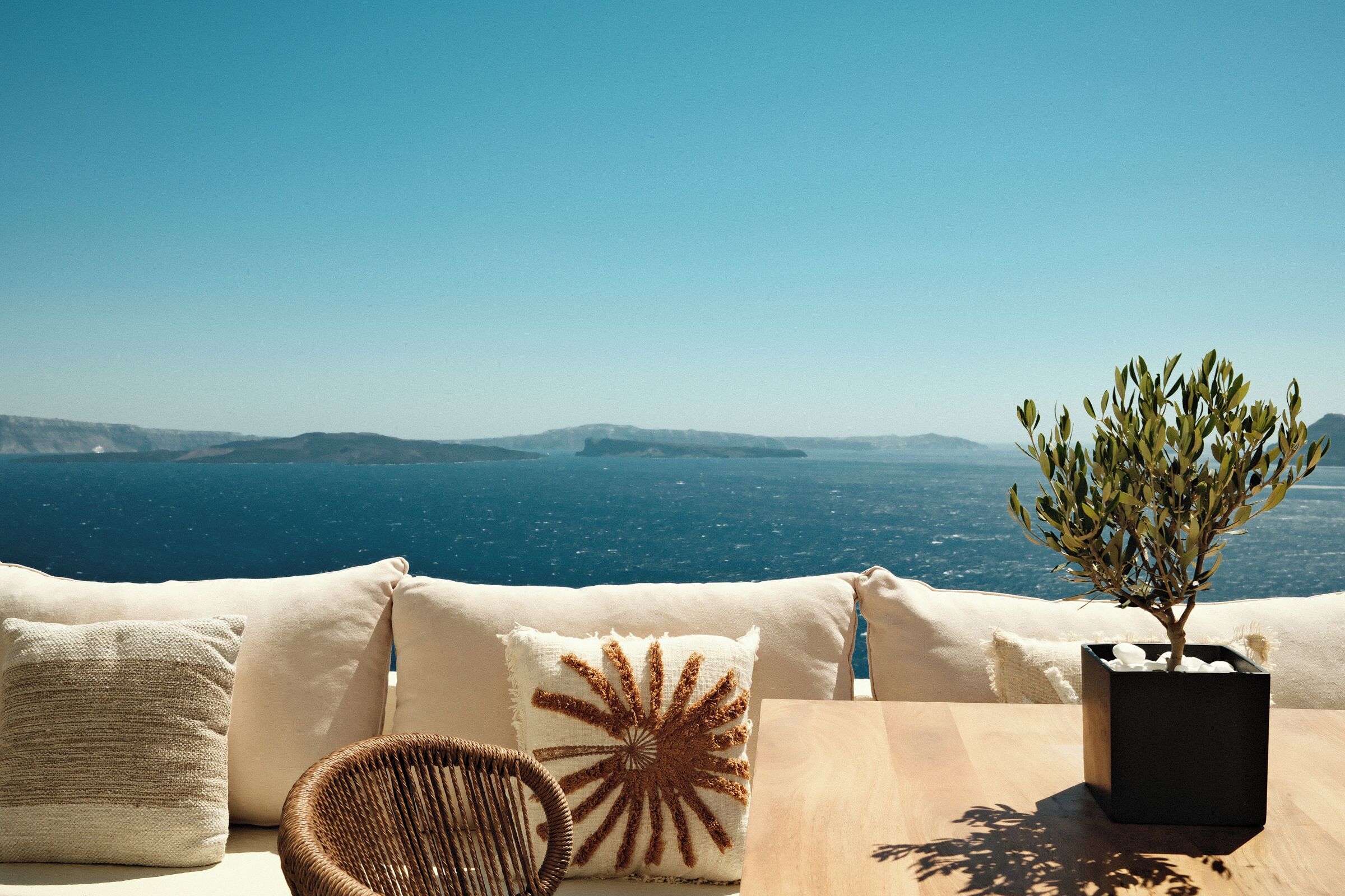 A coastal view with a wooden table, a wicker chair, and a potted plant.