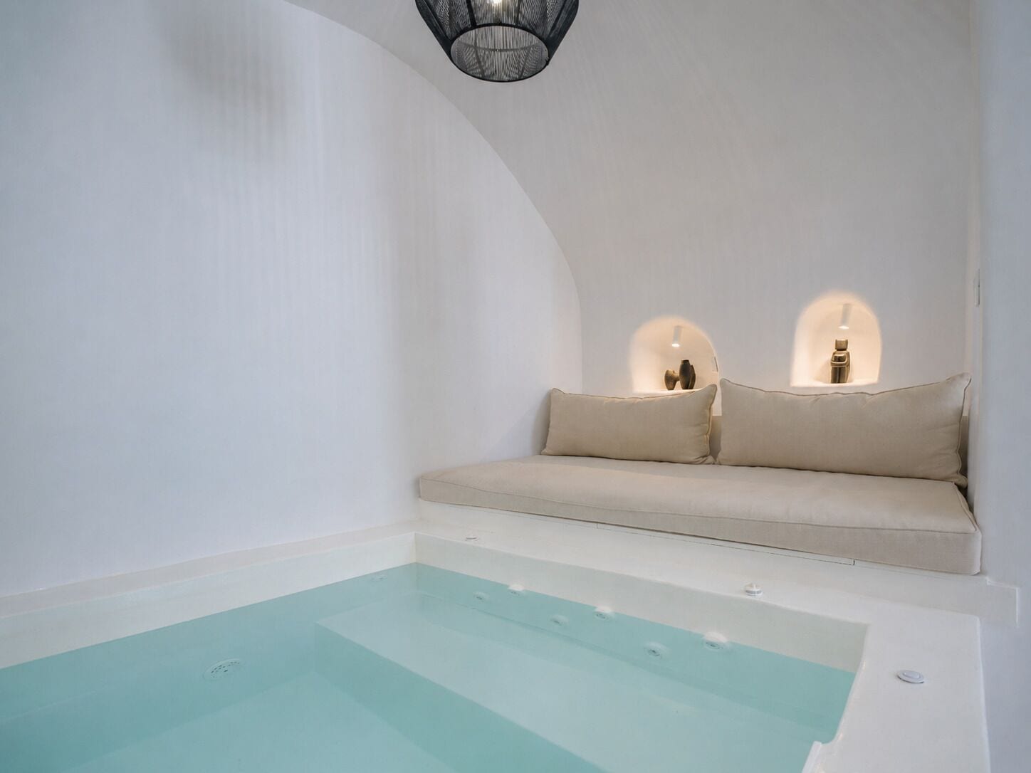 A spa room with a bathtub, a sofa with cushions, and a wall-mounted light fixture.