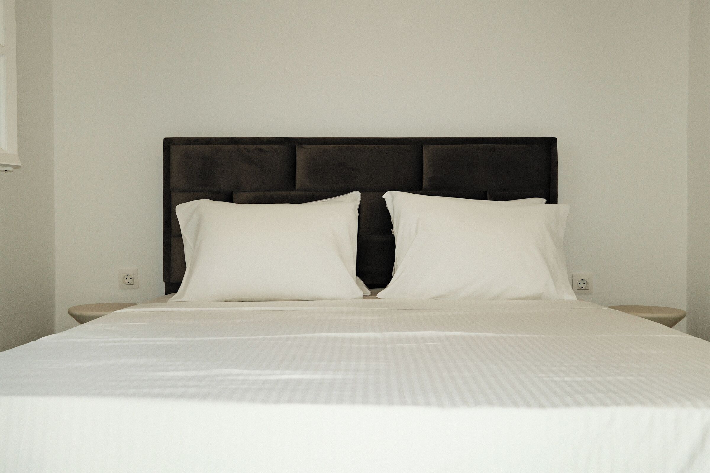Een net opgemaakt bed met een donker hoofdbord en twee witte kussens.