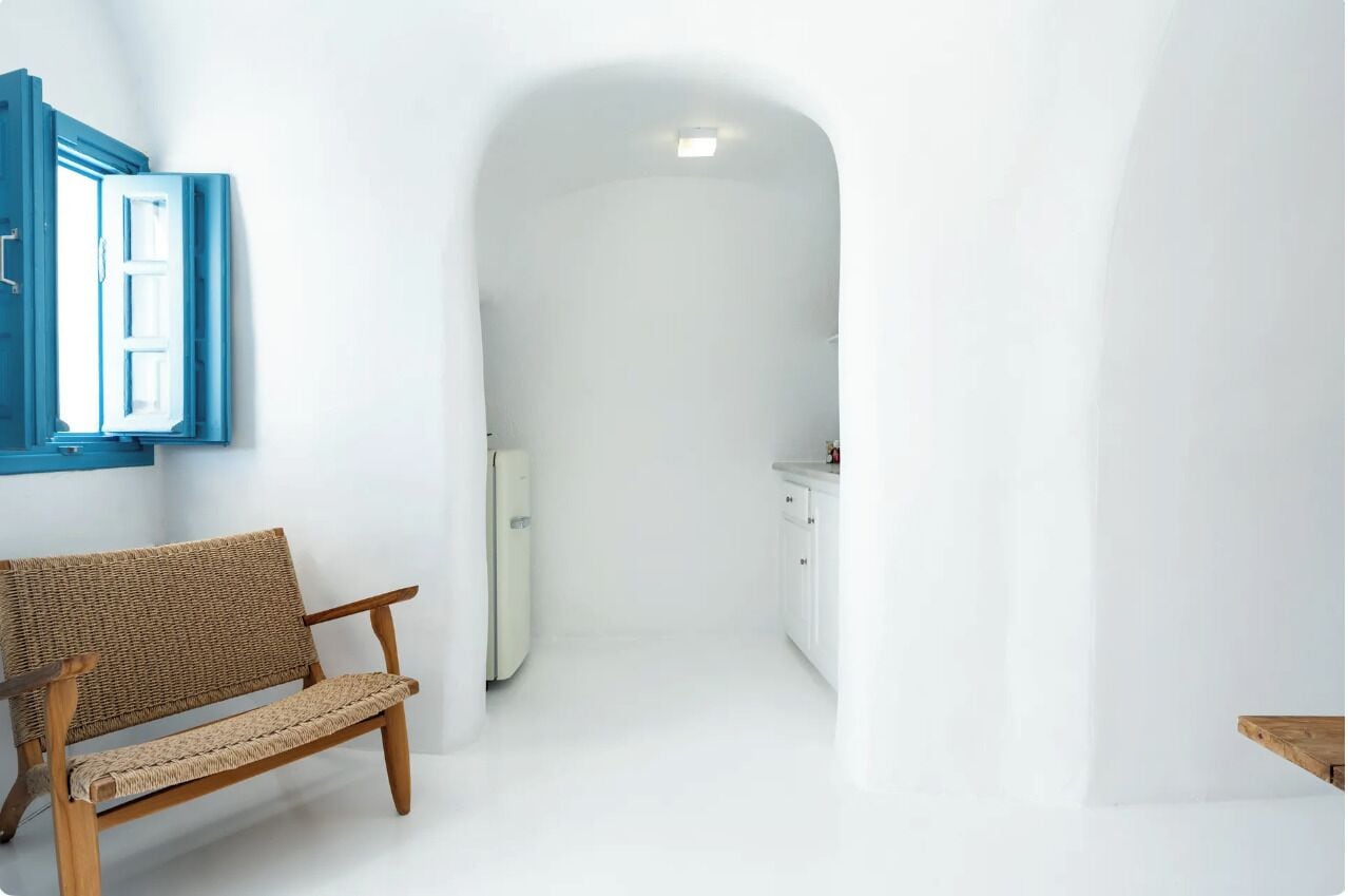 A narrow hallway with a wooden bench on the left, a white door at the end, and a small kitchen area with cabinets and a countertop.