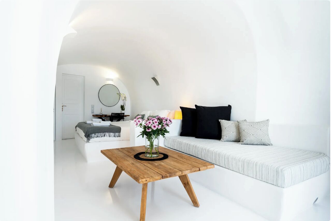 A modern, white-themed living room with a wooden coffee table, a sofa with patterned cushions, and a small side table with a vase of flowers.