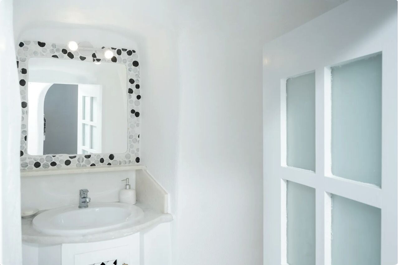 Un baño con lavamanos blanco, un espejo con marco de mosaico y puertas de vidrio esmerilado.
