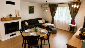 Et spiseområde med et rundt bord dækket til fire personer, en pejs, en sofa og et vindue med gardiner.