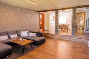 A modern living room with a sectional sofa, a wooden coffee table, and a dining area with a table and chairs. - Holiday house by the Korana River with a jacuzzi, sauna, and a view of the old town of Barilović (Barilović)