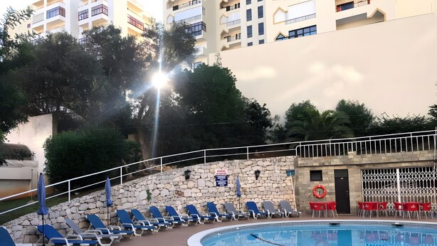 A pool area with lounge chairs and a stone wall. - Apartment 'T2 Premium' with Shared Pool, Wi-Fi and Air Conditioning (Portimão)