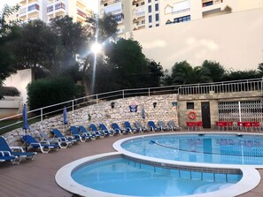 Un área de piscina con sillones de descanso y un muro de piedra.