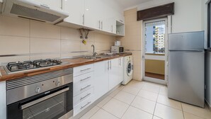 A modern kitchen with a gas stove, oven, washing machine, and a refrigerator. - Apartment 'T2 Premium' with Shared Pool, Wi-Fi and Air Conditioning (Portimão)