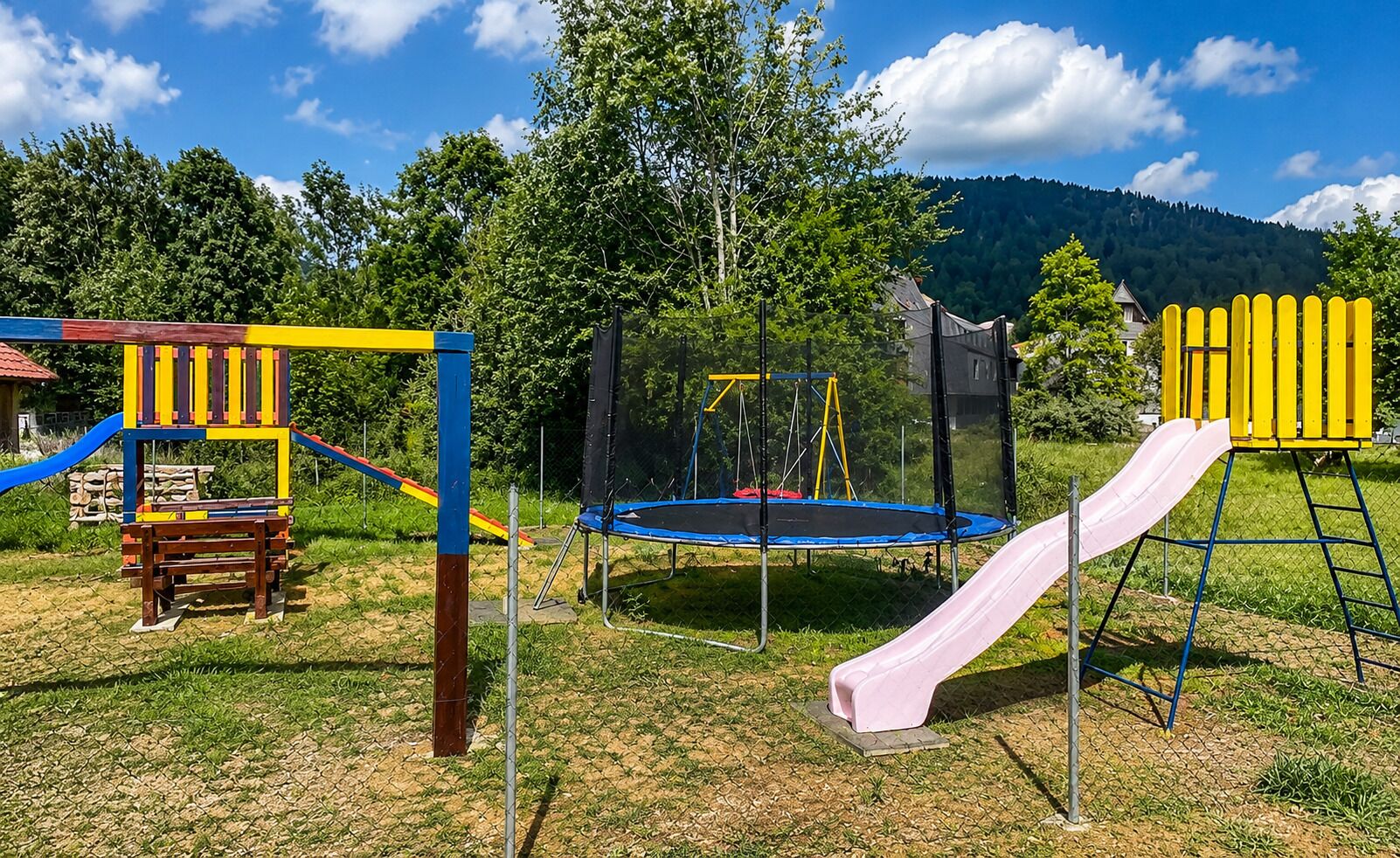 A playground with a slide, swing set, and trampoline.