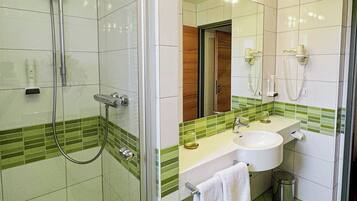 A bathroom with a shower, sink, mirror, and green-tiled floor.