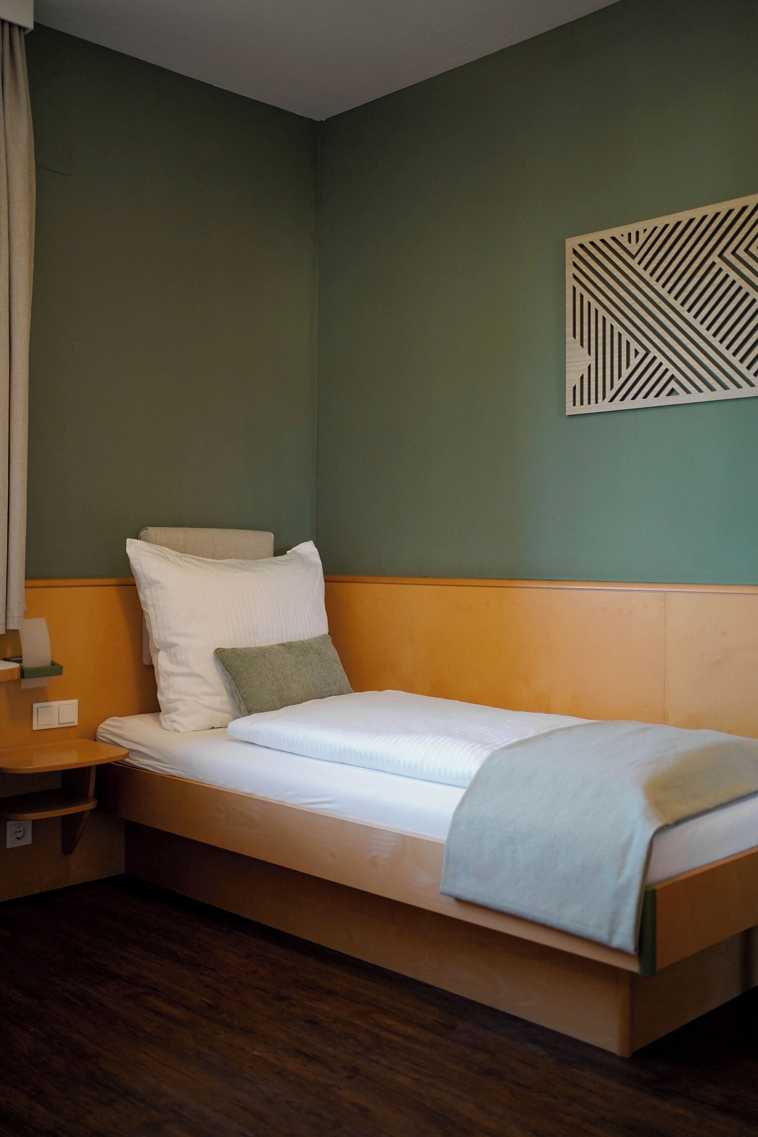 A single bed with a wooden headboard, a nightstand with a lamp, and a wall-mounted geometric decoration.
