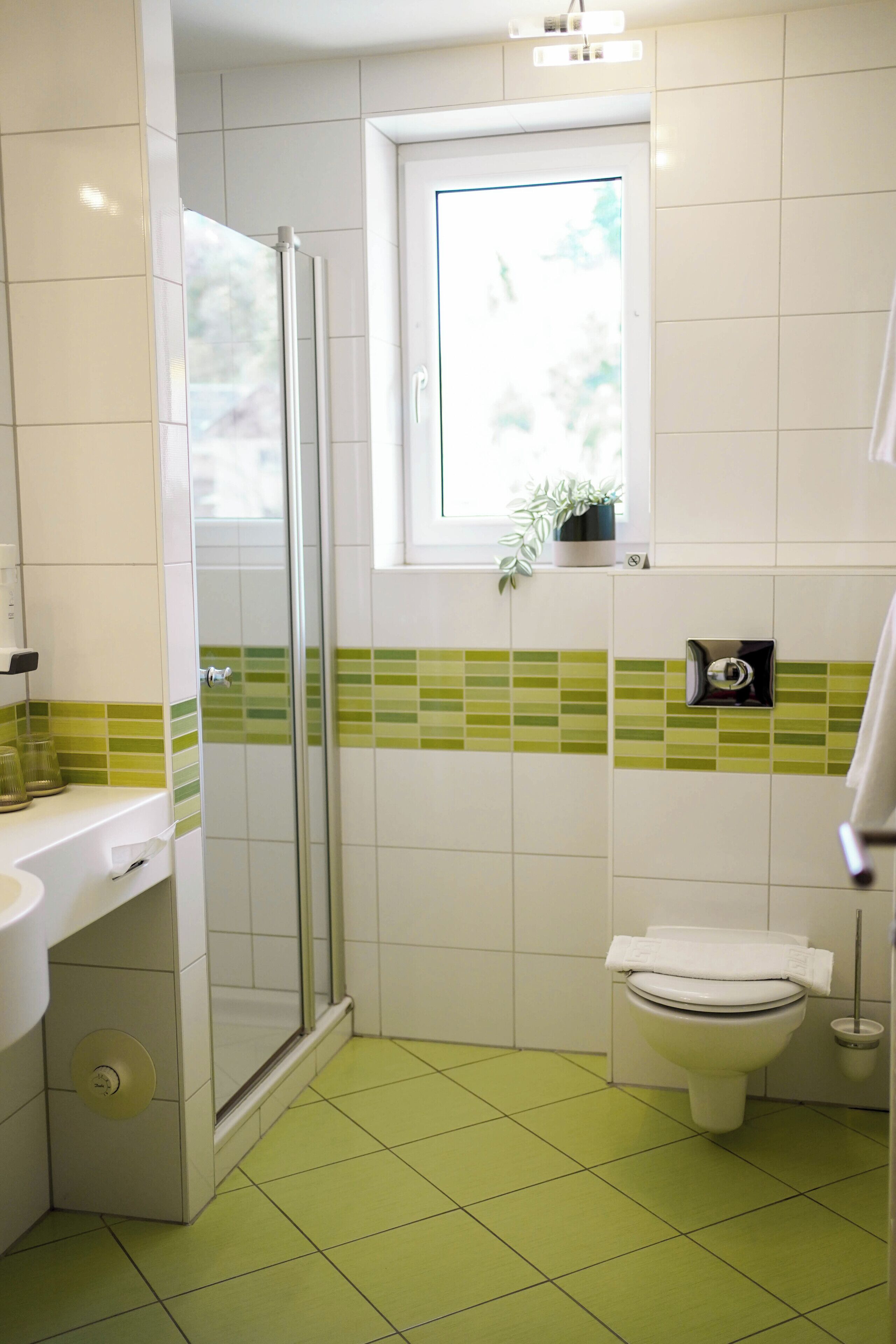A bathroom with a shower, toilet, sink, and a window with a plant.