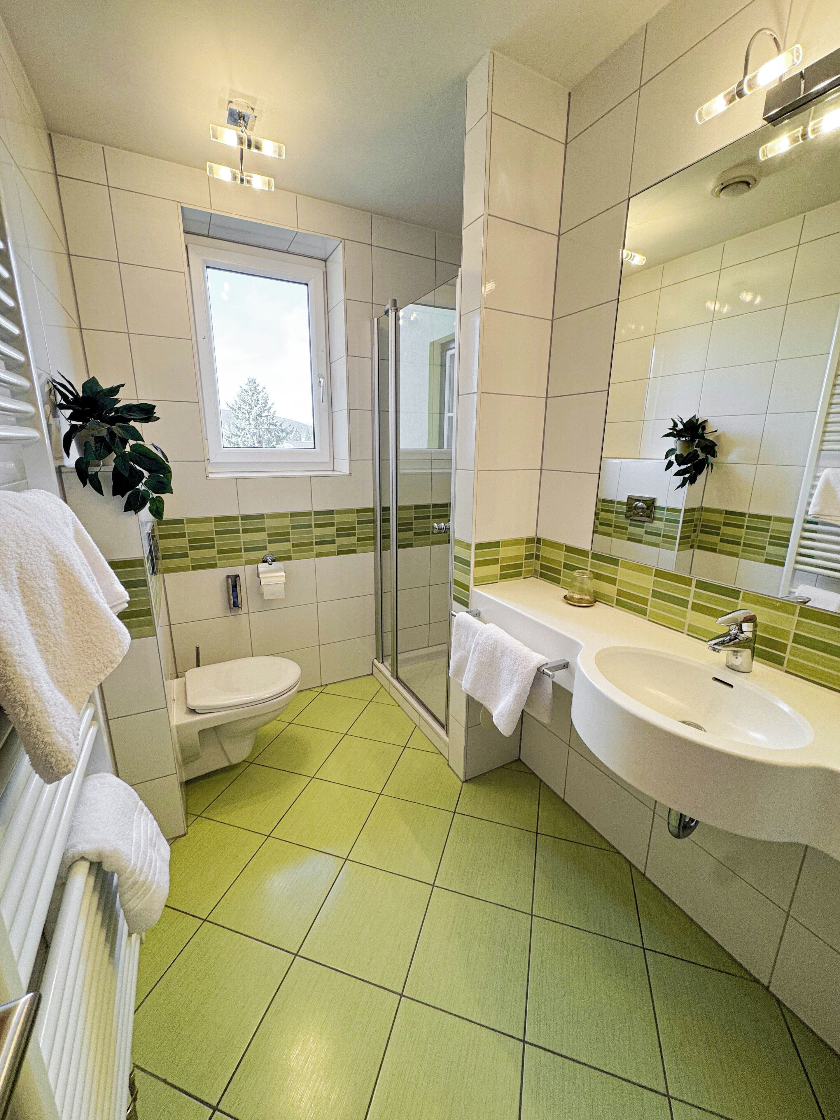Een badkamer met toilet, douche, wastafel en een raam.