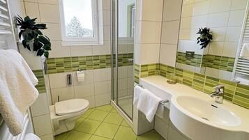 Een badkamer met toilet, douche, wastafel en een raam.