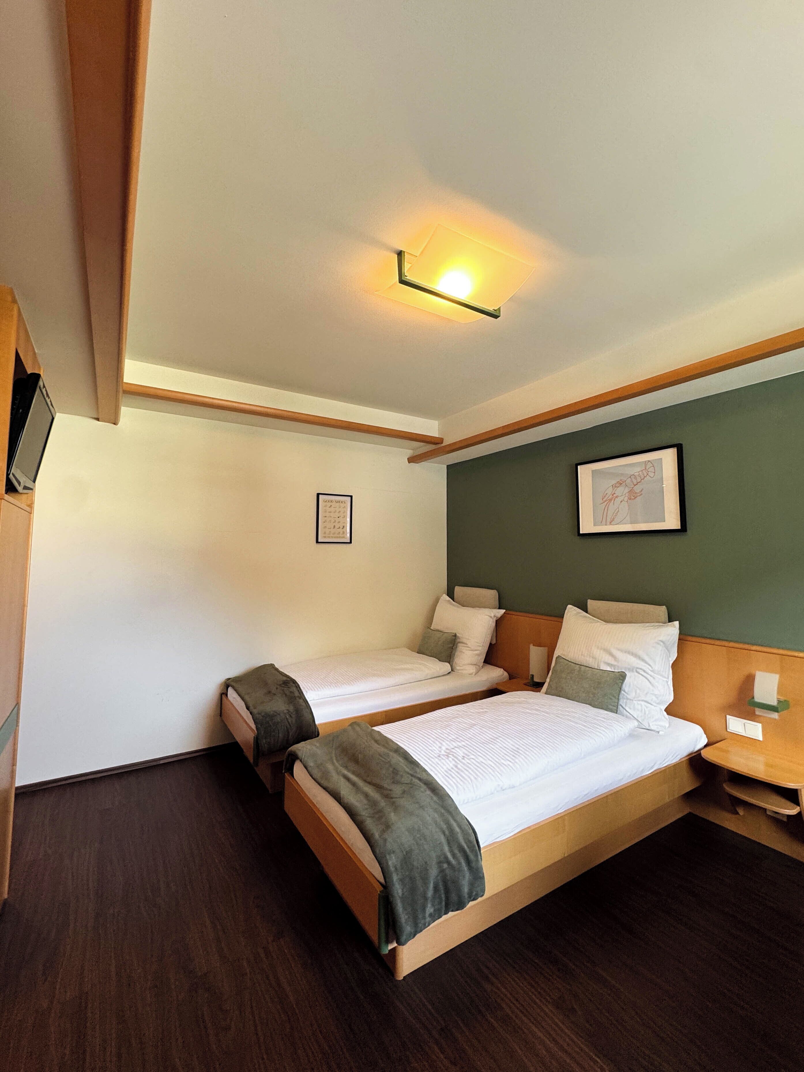 A hotel room with two beds, a nightstand, a lamp, a framed picture, and a ceiling light fixture.