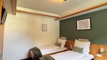 Quarto de hotel com duas camas, uma mesa de cabeceira, abajur, quadro emoldurado e luminária no teto.