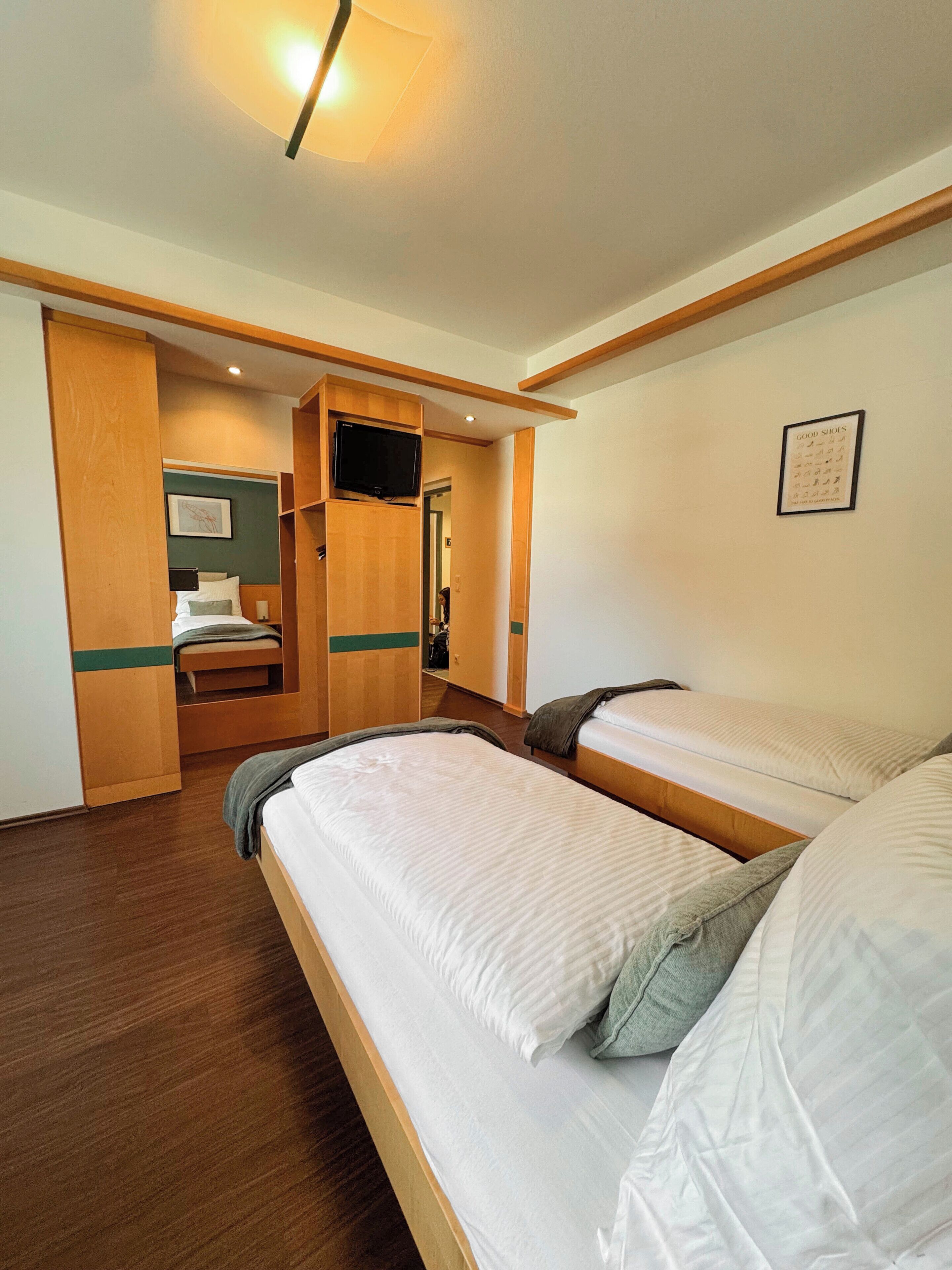 Habitación de hotel con dos camas, un televisor, un armario de madera y una cita enmarcada en la pared.