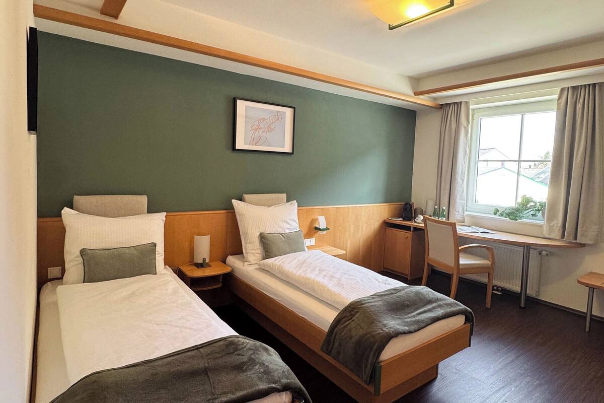 Une chambre d’hôtel avec deux lits, un bureau, une chaise et une fenêtre avec des rideaux.