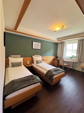 Une chambre d’hôtel avec deux lits, un bureau, une chaise et une fenêtre avec des rideaux.