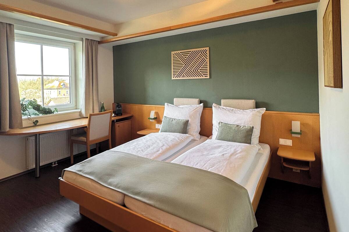 Une chambre d’hôtel avec un grand lit, un bureau, une chaise, une fenêtre avec des rideaux et une œuvre d’art accrochée au mur.