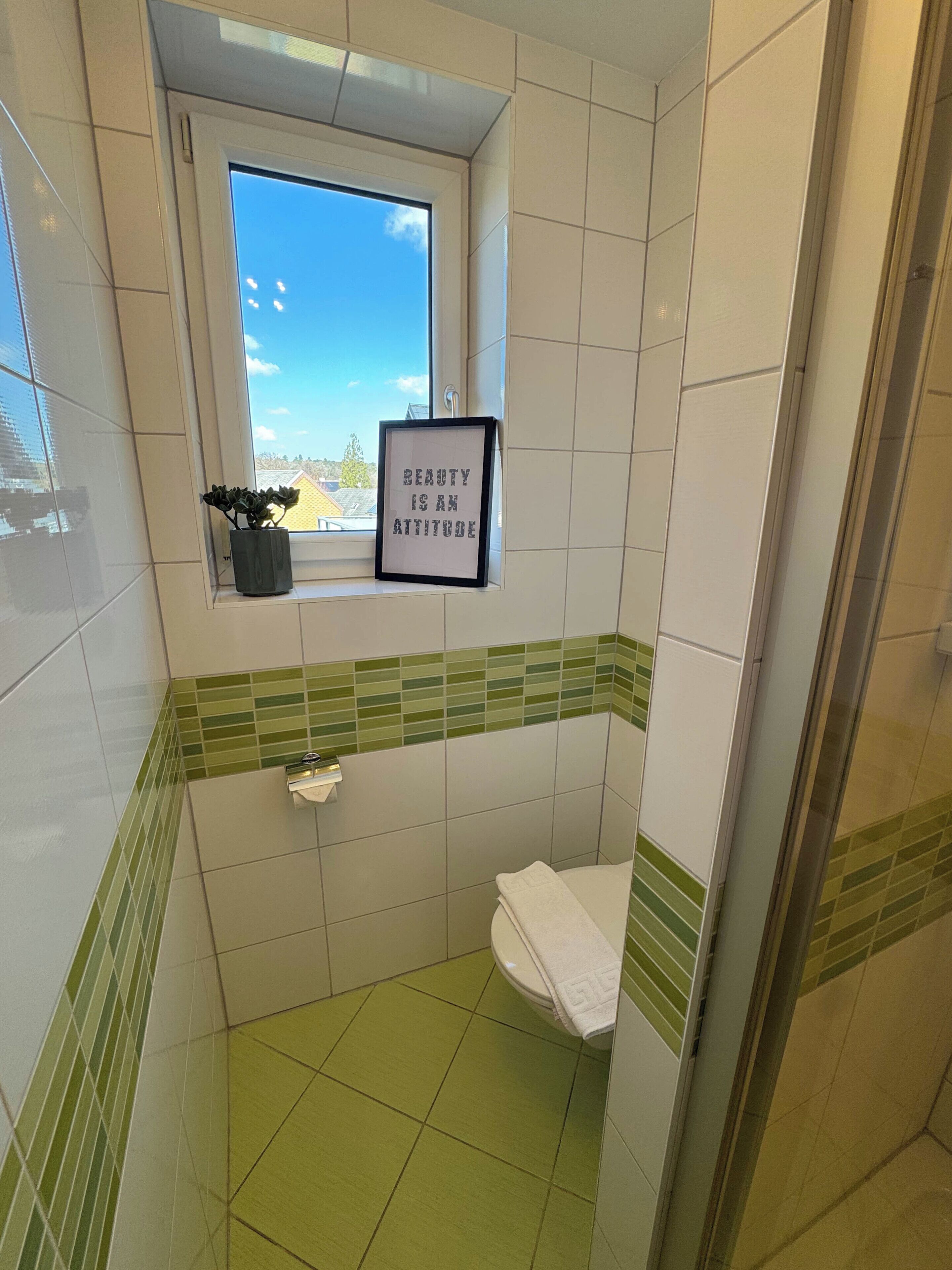 A bathroom with a window, a framed quote, a potted plant, and a toilet.