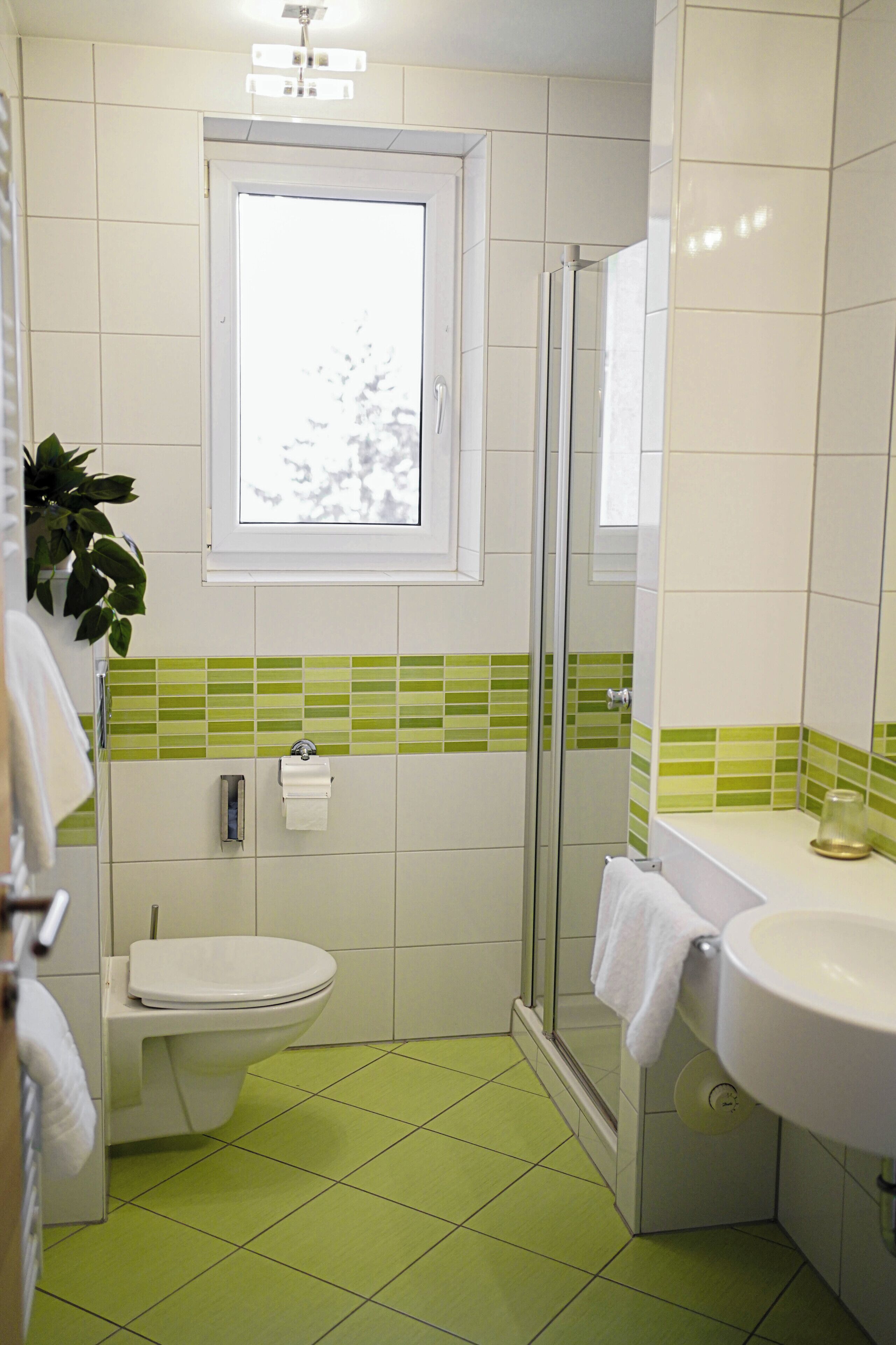 A bathroom with a toilet, a sink, a glass shower enclosure, and a window.