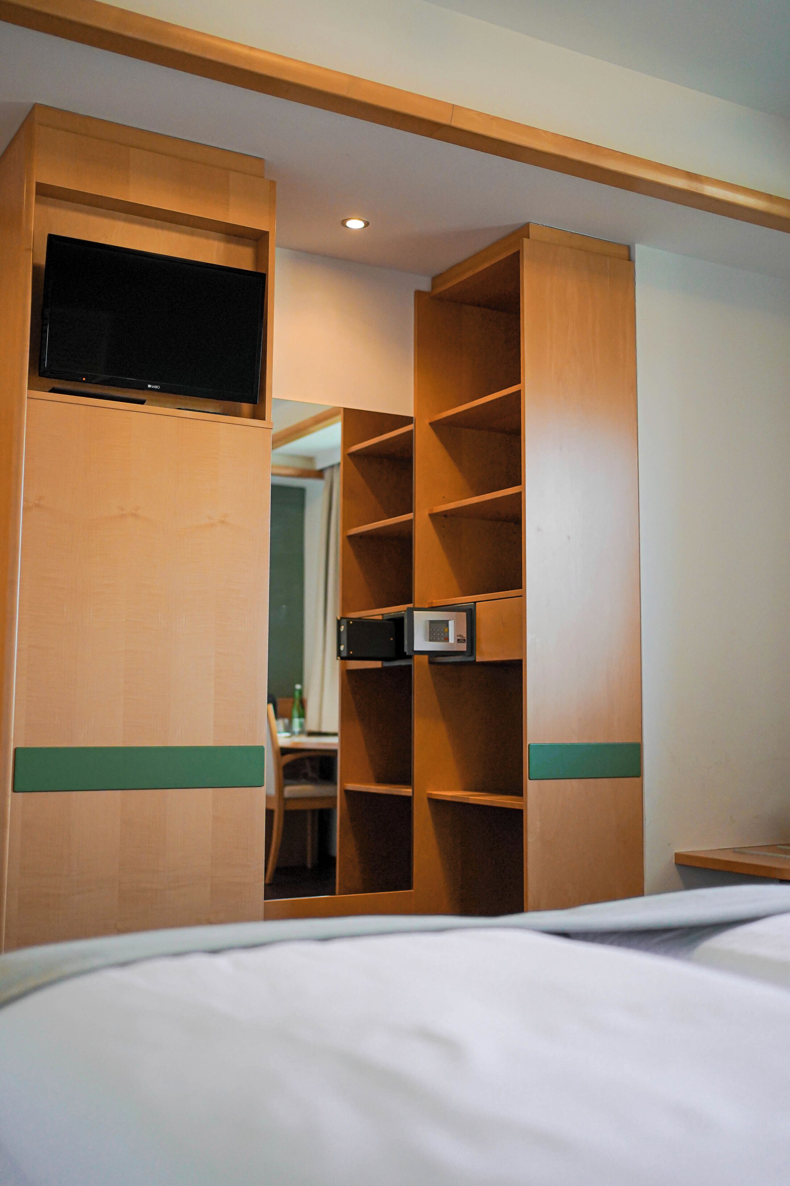 A bedroom with a bed, a wooden wardrobe with shelves, a television, and a microwave.