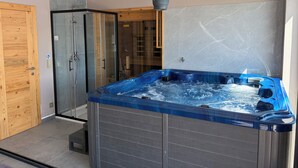 Een moderne badkamer met een douchecabine van glas, een houten deur en een whirlpool.