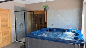 A modern bathroom with a glass shower enclosure, a wooden door, and a hot tub.