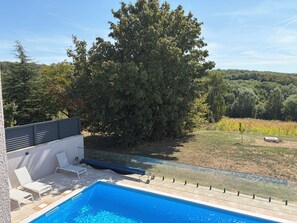 Una piscina con sillas de descanso y un árbol al fondo.