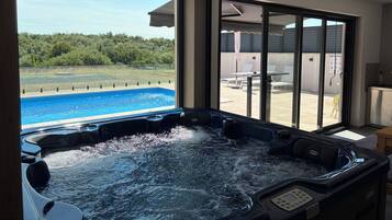 A hot tub with a view of a swimming pool and a patio area with outdoor furniture.