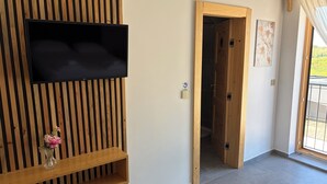 Een kamer met een wandgemonteerde flatscreen televisie, een wand van houten latten, een houten deur en een betegelde vloer.