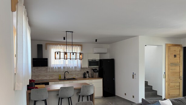 Een moderne keuken met een centraal eiland, barstoelen en een eettafel met een bloevas.